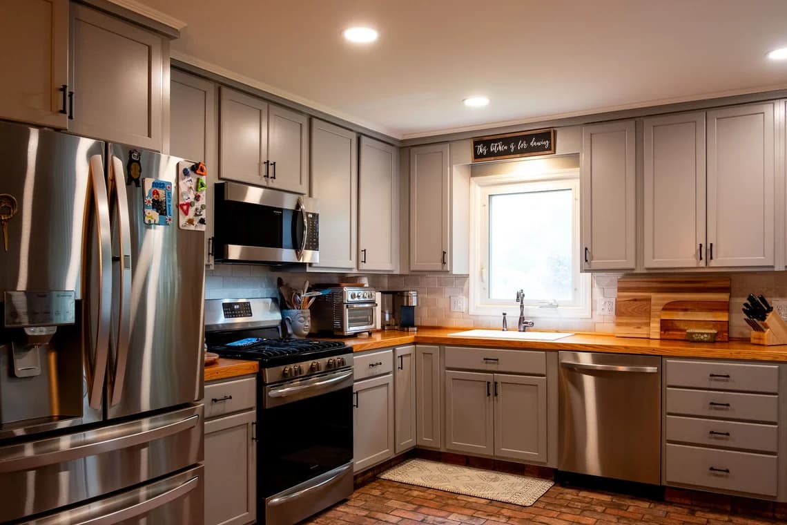 A contemporary kitchen with gray cabinets, stainless steel appliances, and wooden countertops.