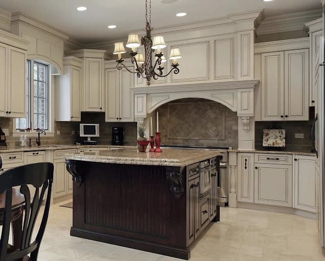 Kitchen cabinet painting project by Anthony Meggs Painting LLC in Monroe, NC. The image shows white cabinets, a dark island, stone counters, and pendant lights.