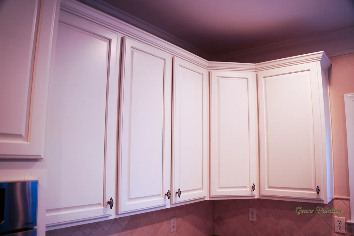 Cabinet painting project by Grace Painting & Contractors in Mooresville, NC. The image shows white upper kitchen cabinets, crown molding, tile backsplash, and wall paint.