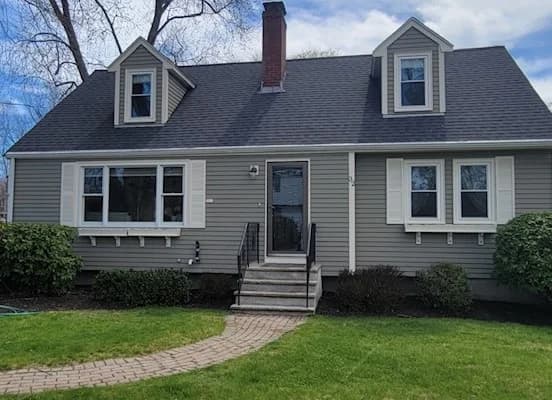 This is an image from CertaPro Painters of North Shore and Cape Ann, located in Massachusetts. The picture displays a gray Cape-style home with white shutters and trim, highlighting the company’s exterior painting work.