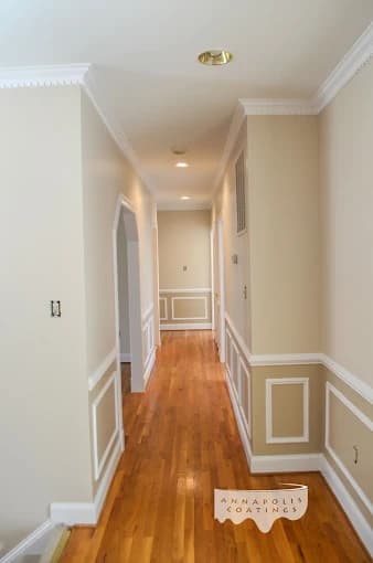 This is an image from Annapolis Coatings, located in Maryland. The hallway interior features freshly painted beige walls with crisp white trim and wainscoting along a polished hardwood floor.
