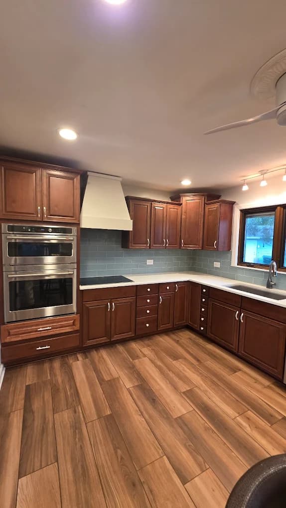 This is an image from Angel the Painter Inc., located in Illinois. The image shows an interior kitchen with stained wood cabinets, gray subway tile backsplash, wood-look flooring, and stainless steel appliances.