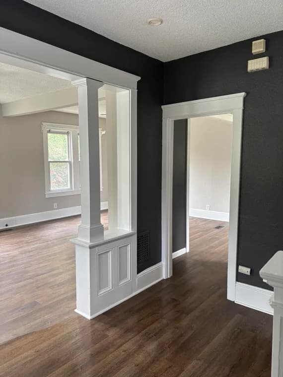 A stylish interior with black accent walls and white trim, painted by WallPro Painting & Design, featuring open columns and wood flooring.