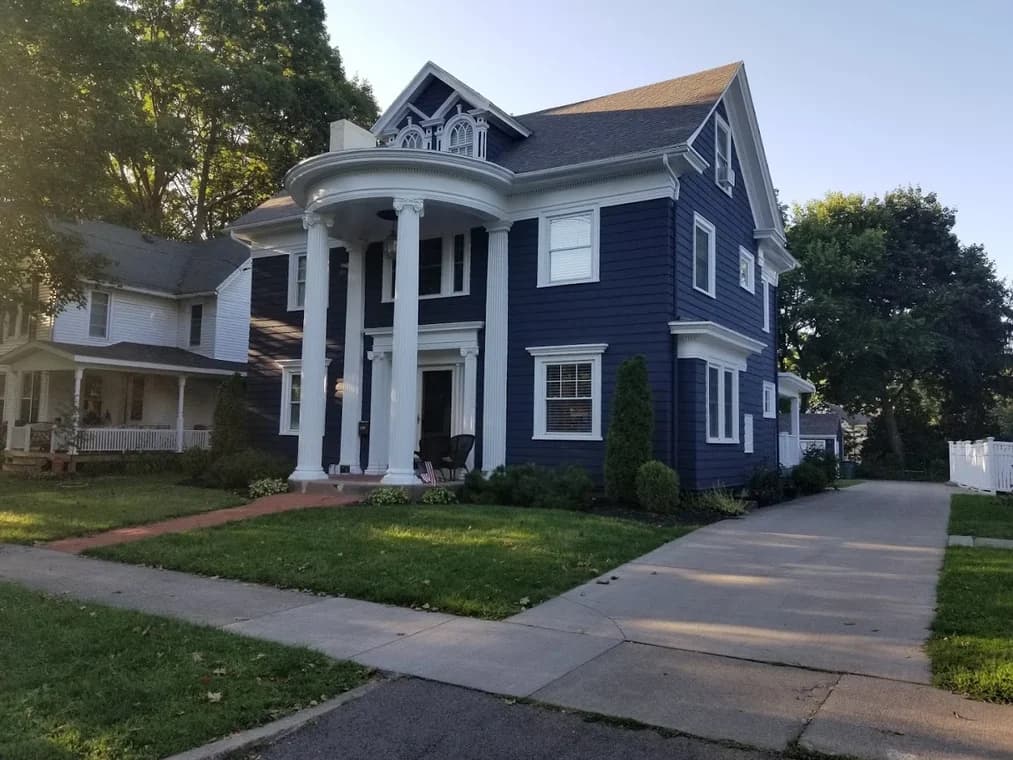 This is an image from A&L Painting, located in New York. The photo shows a large navy blue two-story home with white trim and tall front columns after an exterior painting project