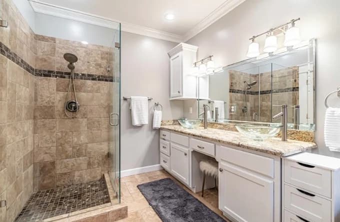 "This is an image from Squared Away Painting, located in Texas. The bathroom includes freshly painted white cabinetry, a large glass shower, granite countertops, and twin glass vessel sinks."