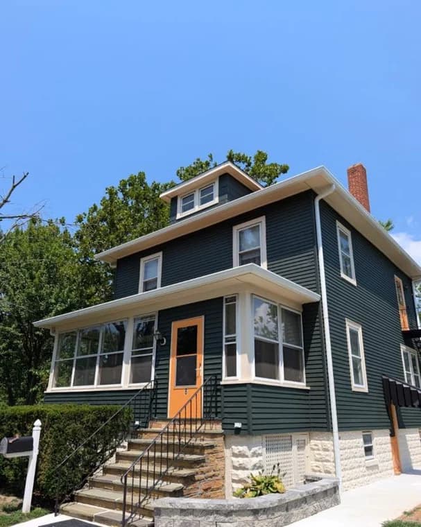 This is an image from Donovan’s Painting, located in Maryland. The photo shows a freshly painted dark green two-story home with white trim and an orange front door under a clear blue sky.