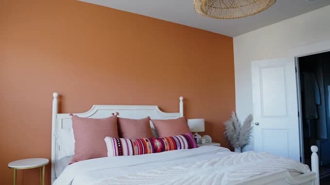 Interior painting project by That 1 Painter Charlotte - Fort Mill in Charlotte, NC. The image shows an orange bedroom wall, white bed, and woven ceiling light.