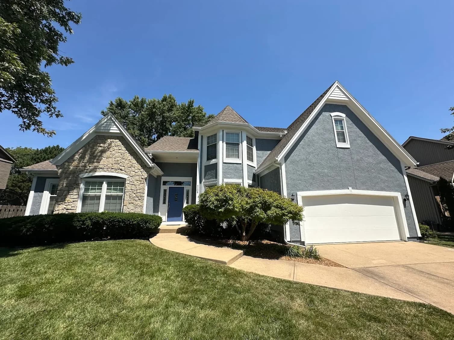 This is an image from Patrick’s Painting. The image shows a freshly painted two-story home with a blue-gray exterior, bright white trim, and a clean white garage door, giving the property an updated and polished curb appeal.