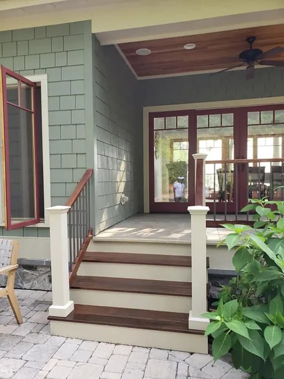 This is an image from Sam Professional Painting LLC, located in Maryland. The photo shows a freshly finished exterior porch entry with painted siding, stained wooden steps, and white railing posts.