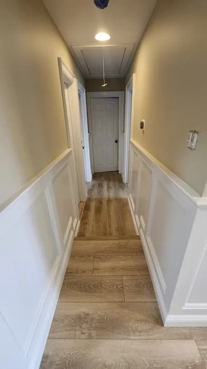 This is an image from CRD Painting Inc, located in New York. The photo shows a hallway with new white wainscoting, beige painted walls, and wood-look flooring