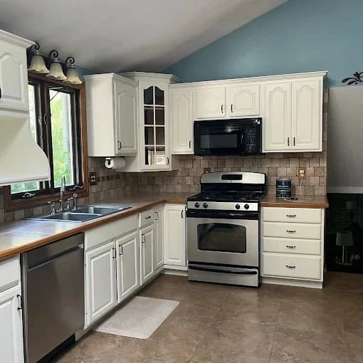 This is an image from Pancione Painting Plus LLC, located in Massachusetts. The photo shows a modern kitchen with white cabinets, stainless steel appliances, and a light blue accent wall.