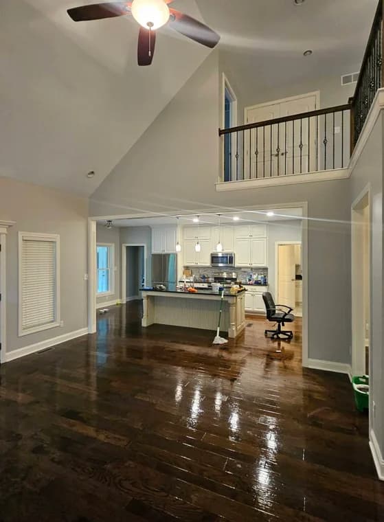 This is an image from Abell Painting LLC, located in Kentucky. The picture shows an open-concept living area with glossy dark wood floors, neutral gray walls, and a view into a bright kitchen with white cabinetry.