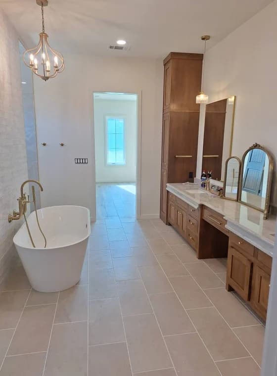"This is an image from Reeves Painting, located in Texas. The bathroom features a freestanding tub, wood cabinetry, tile flooring, and gold fixtures."