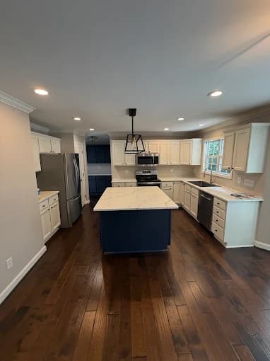 Kitchen painting project by JD Paint Pros LLC in Greensboro, NC. The image shows white cabinets, a navy island, dark wood floors, and pendant lights.