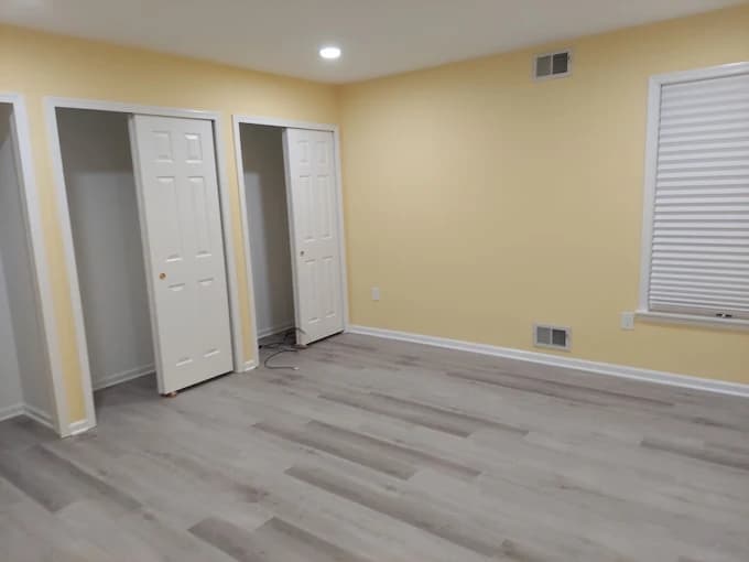 This is an image from Pro Edge Painting, showing a newly painted interior room with pale yellow walls, gray flooring, and white double-door closets. The space is clean and modern with recessed lighting.