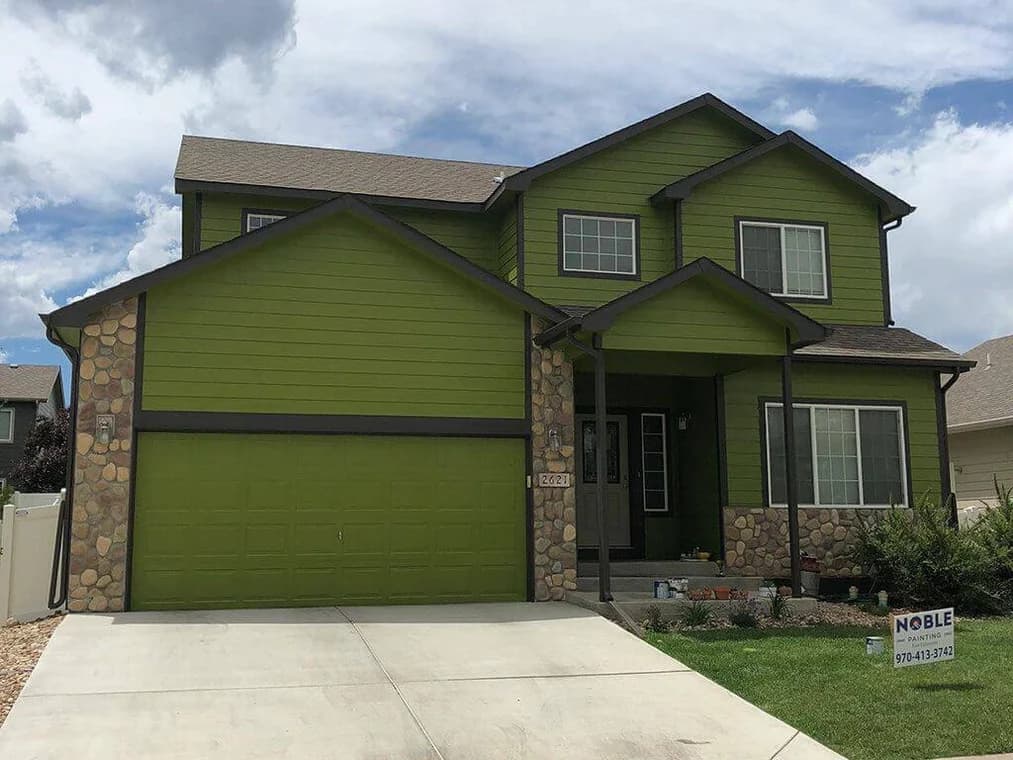 This is an image from Noble Painting company, located in Fort Collins, CO The image is a two-story suburban home with vibrant green exterior siding, stone accents, and dark trim, freshly painted by Noble Painting with job sign visible in front yard