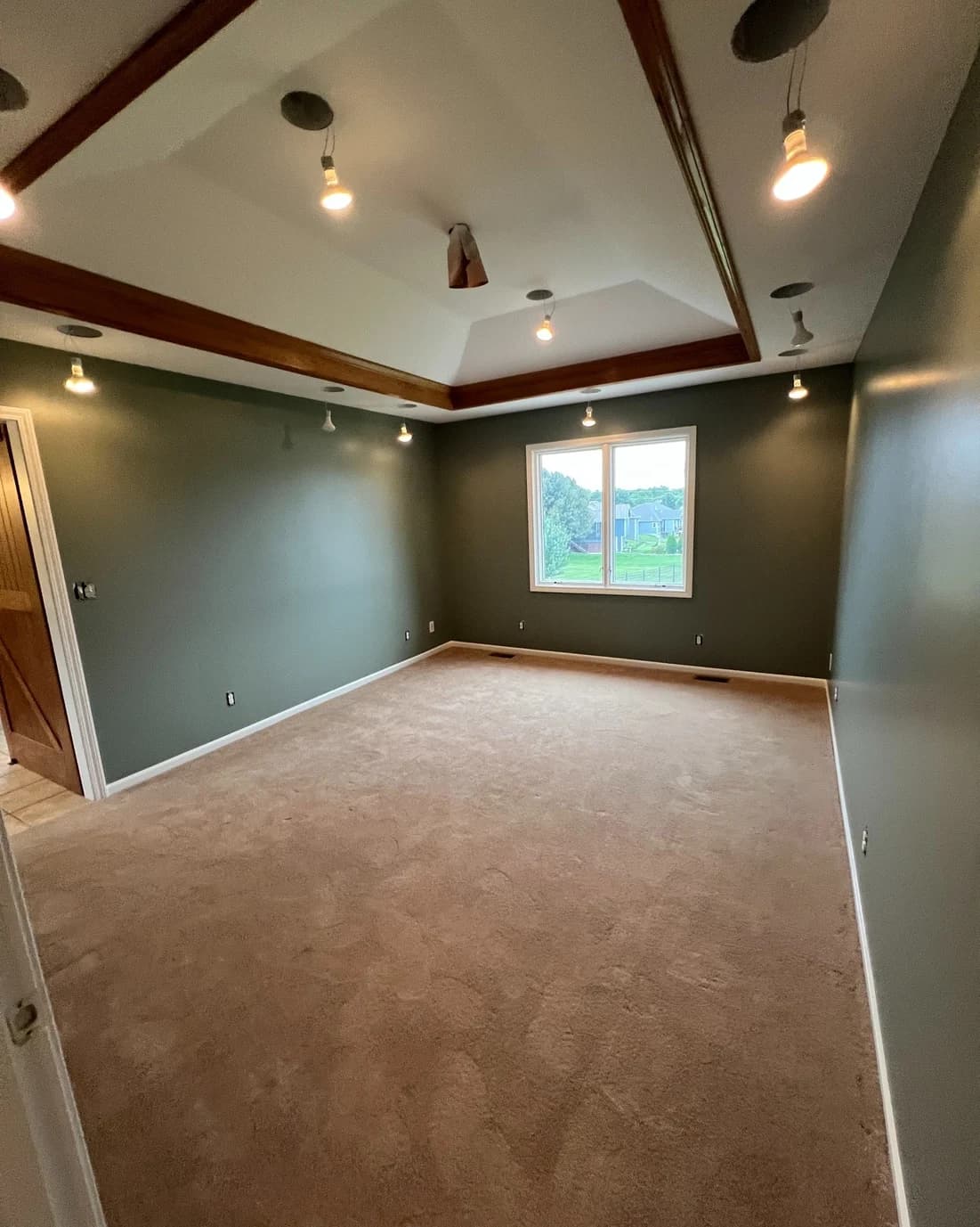 This is an image from Graystone Painting and Refinishing. The image is an interior bedroom in Kansas City KS with newly painted green walls, recessed lighting, and a tray ceiling with wood beam accents.