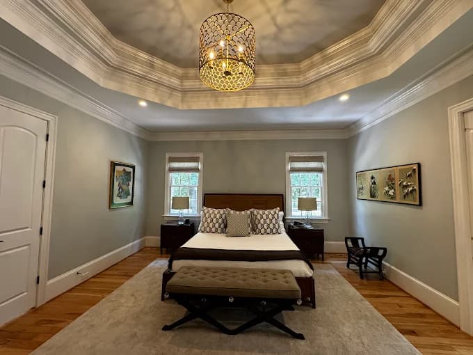 Interior painting project by Triangle Pro Painting in Raleigh, NC. The image shows a bedroom with gray walls, white trim, wood flooring, and a chandelier.