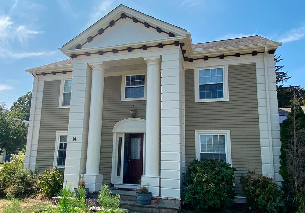 This is an image from Zuck Painting, located in Massachusetts. It shows the exterior of a two-story home with beige siding, large white columns, and neatly painted trim.