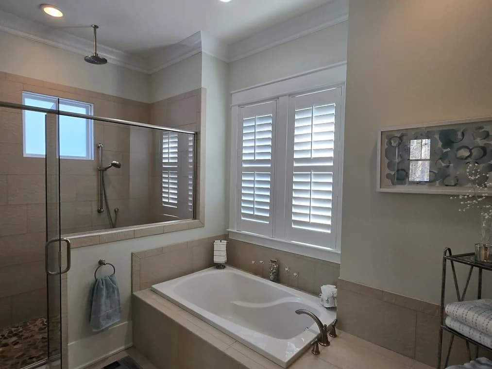 Interior painting project by Freedom Painting in Wilmington, NC. The image shows a bathroom with beige tile, white shutters, and a tub.