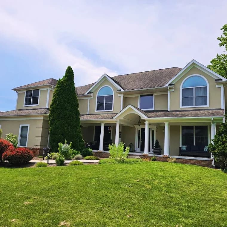 This is an image from CAZ Paintz LLC, located in New York. The photo shows a large beige two-story home with fresh exterior paint, white trim, and a landscaped front yard.