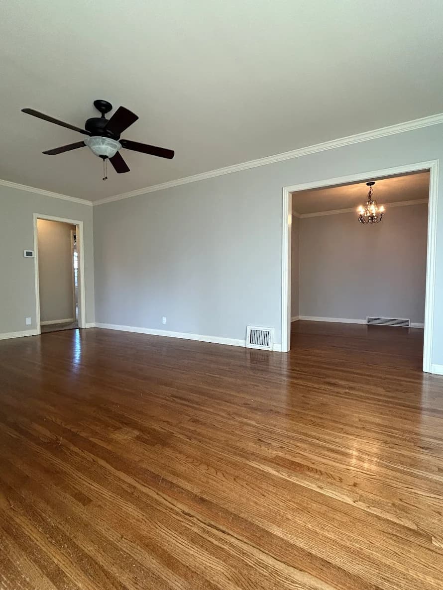 This is an image from Koehn Painting Co LLC. The image shows an interior room with smooth light-gray walls, bright white trim, and refinished hardwood floors, creating a clean and modern living space with a warm, polished appearance.