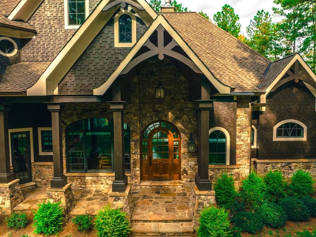 Exterior painting project by Grace Painting & Contractors in Mooresville, NC. The image shows a stone home with dark siding, trim, porch columns, and arched windows.