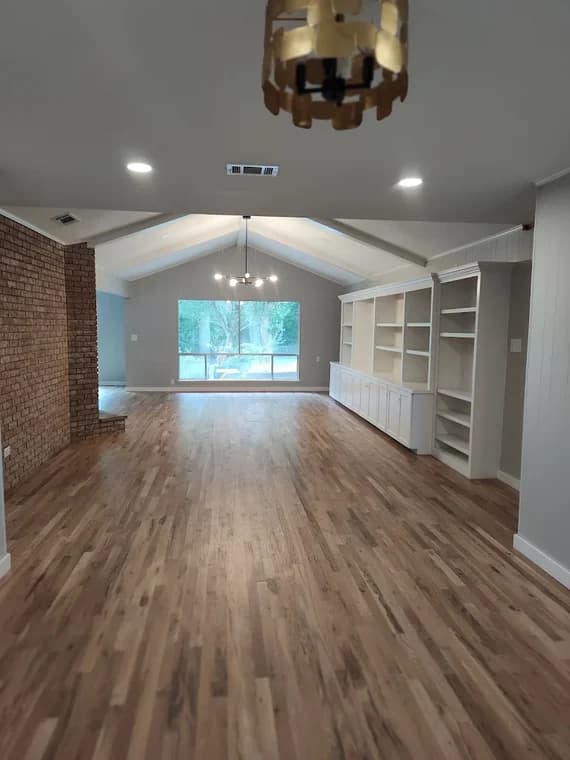 "This is an image from Hutch-N-Son Painting & Drywall, located in Texas. The photo shows a large living area with newly refinished wood floors, painted walls, built-in shelving, and updated recessed lighting."