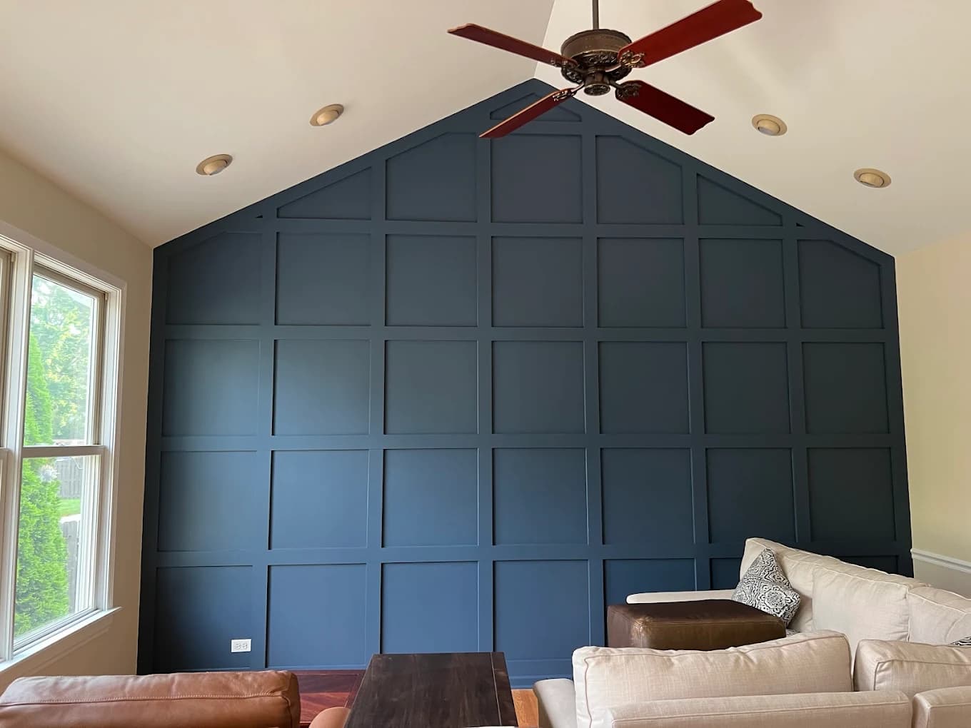 Interior painting project by Jung Family Painting in Naperville, IL. The image shows a dark blue paneled accent wall, vaulted ceiling, fan, and seating.