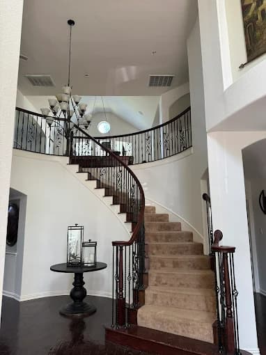 This is an image from MJ Workforce Solutions LLC, located in Texas. The photo shows an elegant interior staircase with dark wood railing, carpeted steps, and a large decorative chandelier above.