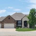 This is an image from West & Co Painting, LLC. The image shows a brick and stone home with dark trim, a three-car garage, and a well-kept lawn.