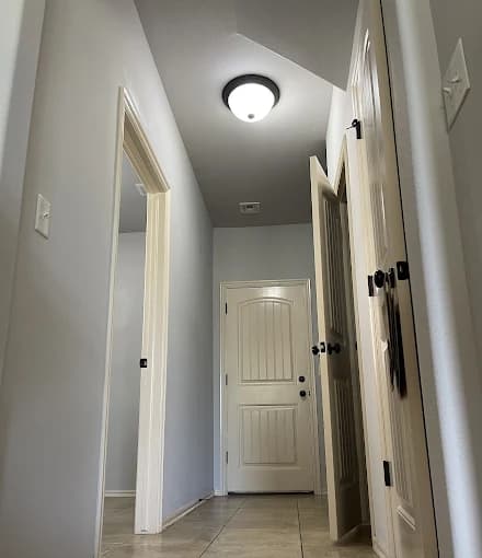 This is an image from Majestic Home Painting, depicting an indoor hallway with soft gray painted walls. The white trim, doors, and ceiling light fixture add a clean and updated appearance.