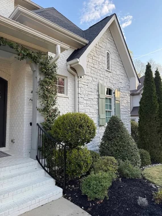 Exterior painting project by GW Painting in Charlotte, NC. The image shows white siding, porch columns, dark shutters, and trimmed shrubs.