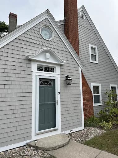 This is an image from CertaPro Painters of Cape Cod, located in Massachusetts. The photo shows a Cape-style home with light gray shingle siding, crisp white trim, and a teal front door, creating a welcoming and polished exterior finish.