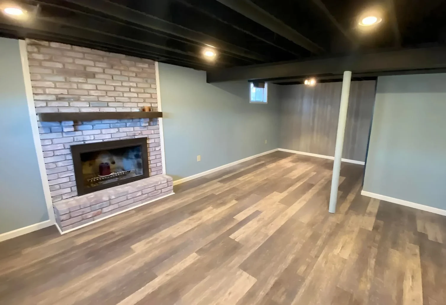 This is an image from Neighborhood Painting and Restoration. The image is finished basement in Kansas City KS with painted brick fireplace and new wall color