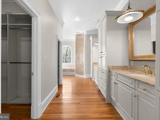 This is an image from Julio's Painting LLC, located in Maryland. The image shows a bright hallway featuring hardwood floors, built-in cabinetry, and a vanity area with a gold-framed mirror.