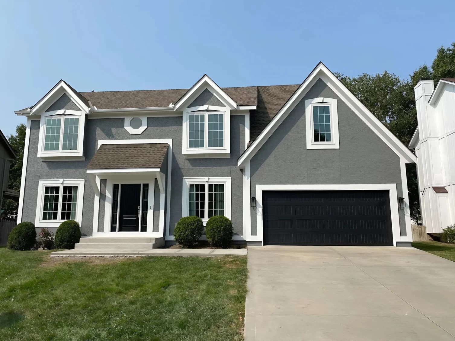 This is an image from Neighborhood Painting and Restoration. The image is two-story gray home in Kansas City KS with sharp white trim and fresh exterior paint