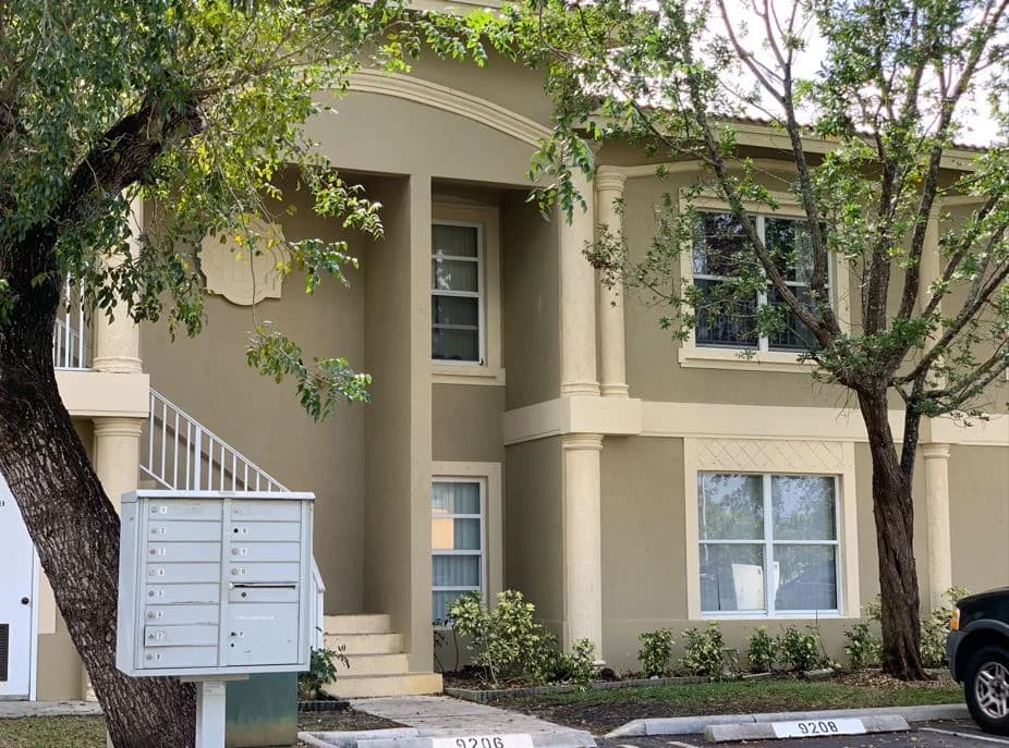 This is an image from Promax Painters company, located in Boynton Beach, FL. The image is a two-story tan and cream stucco apartment building with fresh exterior paint, decorative columns, and trimmed landscaping