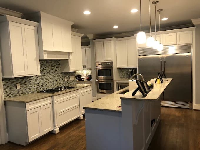 Kitchen cabinet painting project by Roca's Painters LLC in Mebane, North Carolina. The image shows white cabinets, stone counters, and island pendant lights.