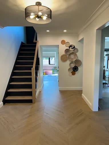 This is an image from Elite Painting Services Plus, located in New York. The hallway showcases a modern staircase with black treads, light wood accents, herringbone tile flooring, and decorative wall art.