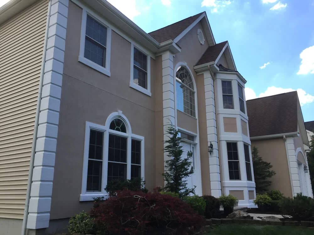 Two-story stucco and siding house with beige walls, accented by white trim columns and window frames, painted by Touch of the Brush Painting.