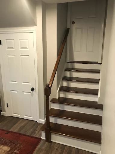 This is an image from Paul’s Painting & Powerwashing, located in New Jersey. The image shows an interior staircase with dark wood treads, white risers, and freshly painted surrounding walls and doors.