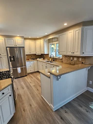This is an image from Todd's Painting, located in New York. The kitchen features newly painted white cabinets, granite countertops, recessed lighting, and light wood plank flooring.