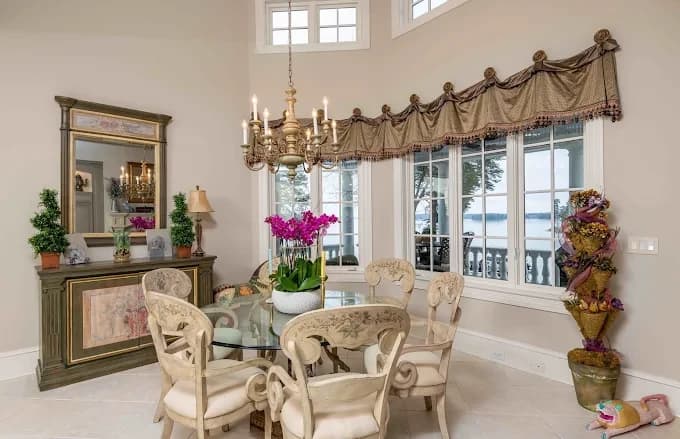 Interior painting project by Trailblaze Paints in Mooresville, NC. The image shows a dining room with high windows, light walls, chandelier, table, and patterned valance.