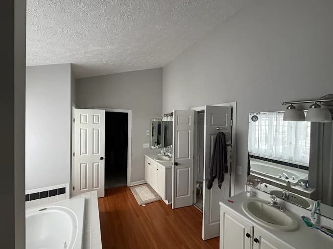 This is an image from Bates Brothers Painting LLC, located in New York. A spacious bathroom with freshly painted gray walls, white vanity cabinets, hardwood flooring, and black-and-white tile accents.