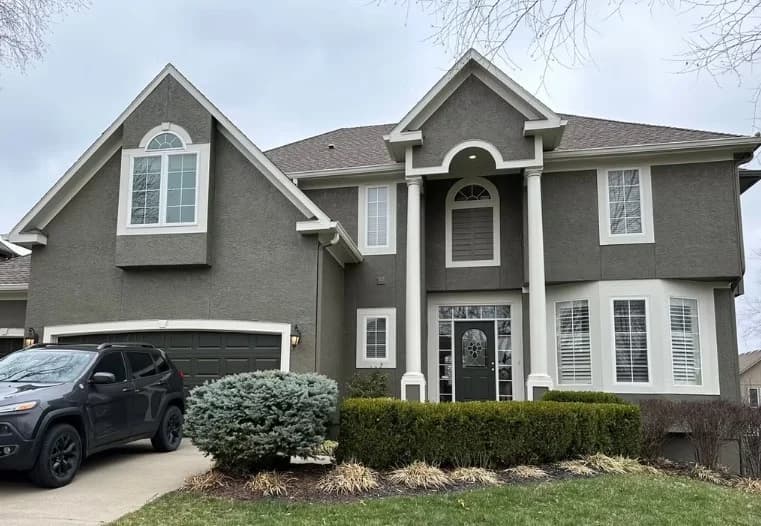 This is an image from Odyssey Painting. The image shows a two-story home with dark gray exterior walls, white trim, and a landscaped front yard.