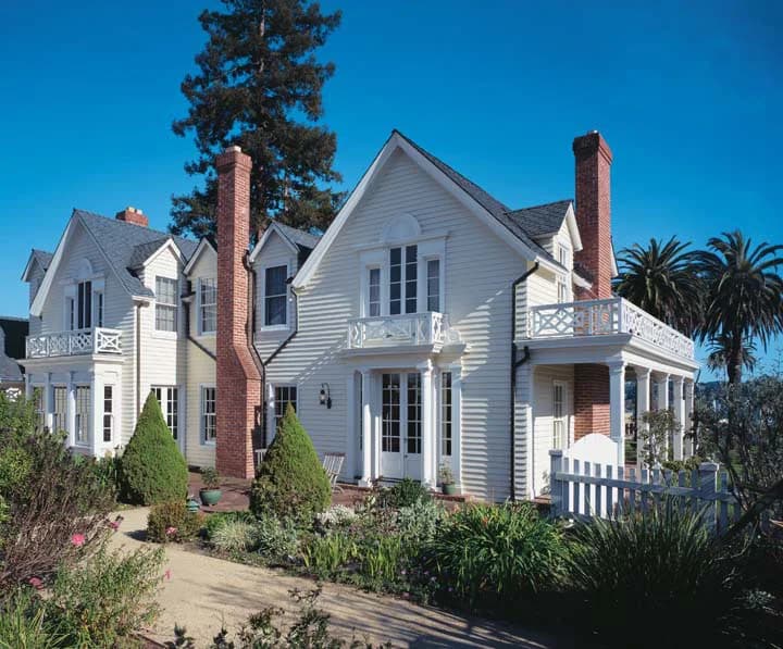 This is an image from CertaPro Painters of San Antonio, located in Texas. The exterior photo shows a large white traditional-style home with brick chimneys and detailed trim work surrounded by landscaped gardens.