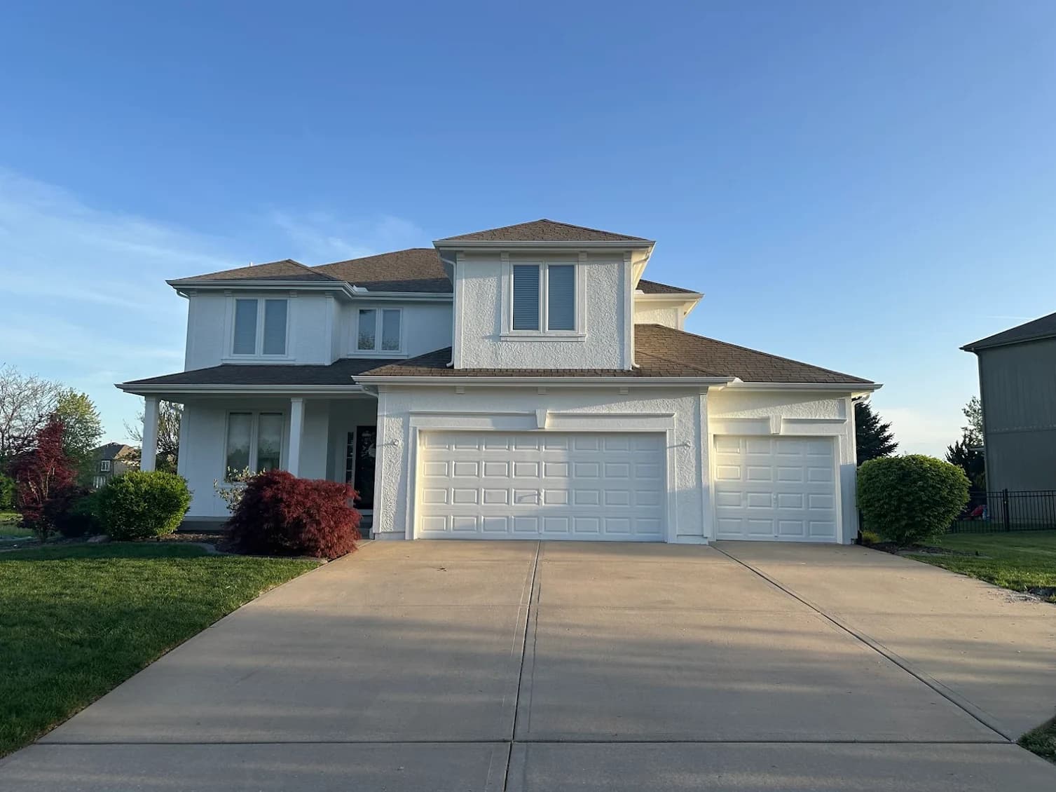 This is an image from 360 Painting of Overland Park. The image shows the exterior of a two-story stucco home in Overland Park KS with a three-car garage and freshly painted white walls.