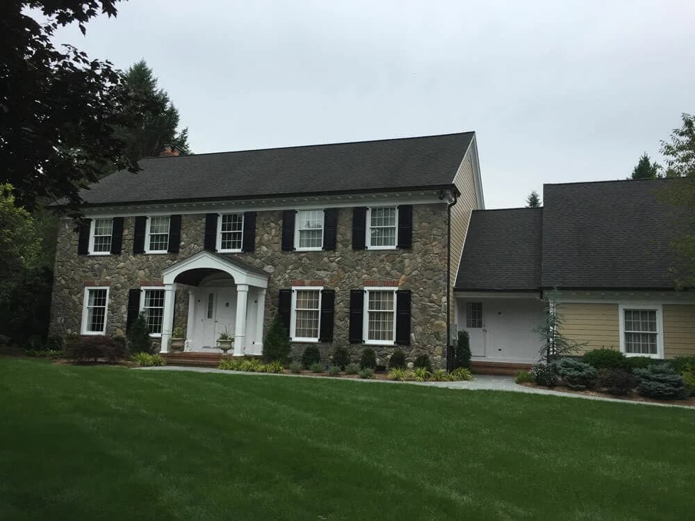 Stone façade home with black shutters and beige siding on the side addition, showing Touch of the Brush Painting’s exterior work.