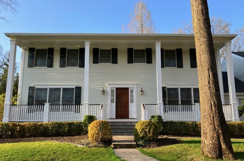 This is an image from J & S Painting Plus, located in New York. The exterior image showcases a large two-story colonial home with light siding, dark shutters, and a full front porch with white railings.